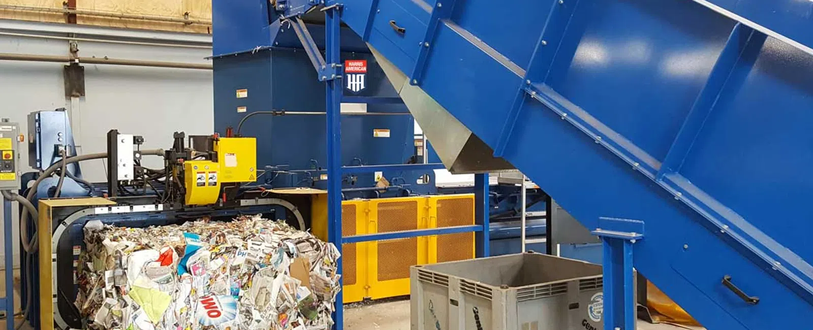Industrial recycling machine compressing mixed paper waste into dense bales inside a processing facility.