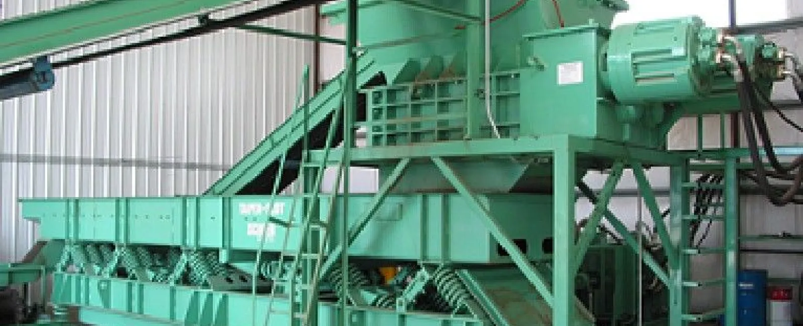 Large green industrial baler machine inside a warehouse with conveyor belt and motor unit