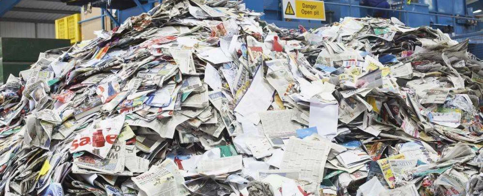 Large pile of shredded and discarded newspapers inside a recycling facility with industrial machinery.