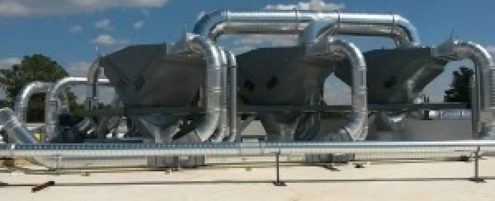 Industrial ventilation system with large metallic ducts and exhaust units on a rooftop under blue sky.