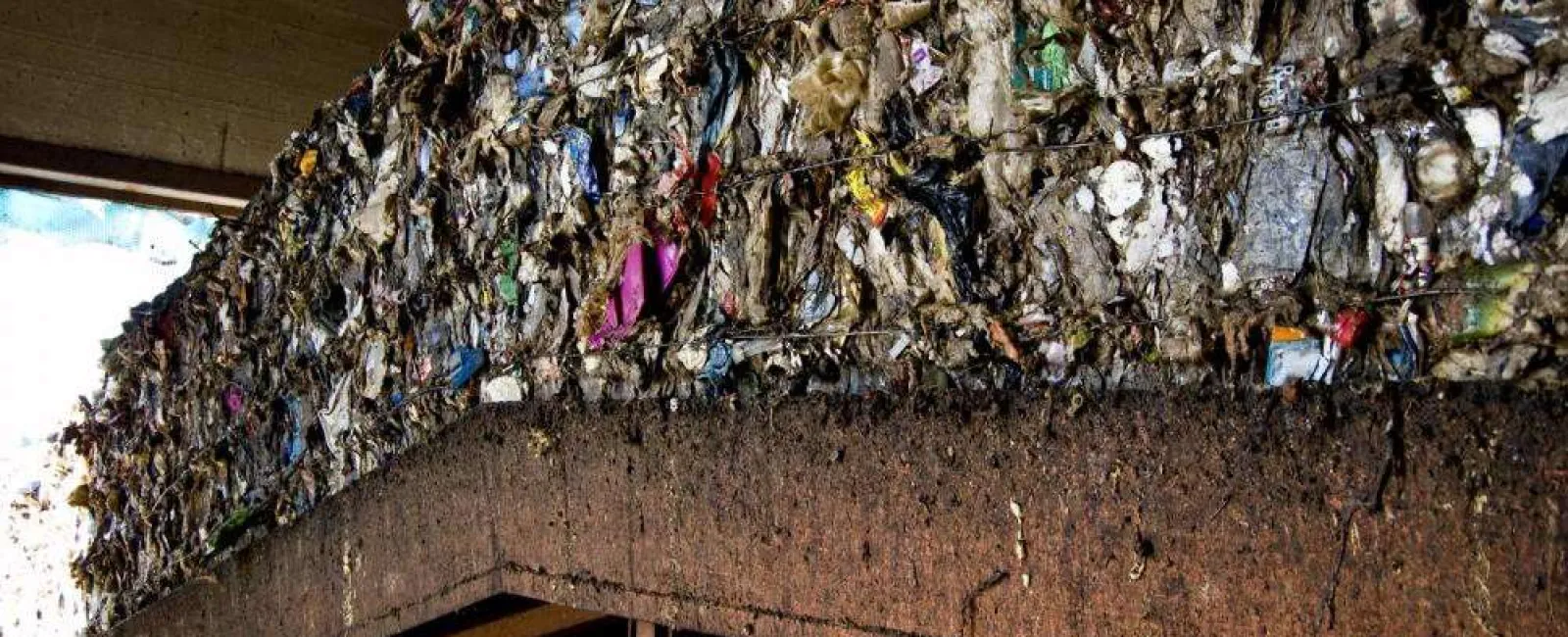 Large compacted bale of mixed recyclable waste including plastics and paper stored in an industrial waste facility.