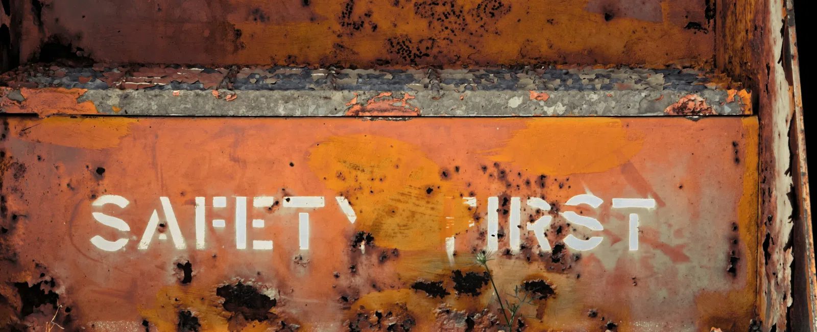 Rusty metal surface with faded white stencil text reading Safety First in an industrial setting.