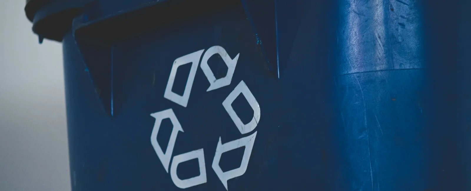 Close-up of a blue recycling bin showing the white recycling symbol on its side for waste management.