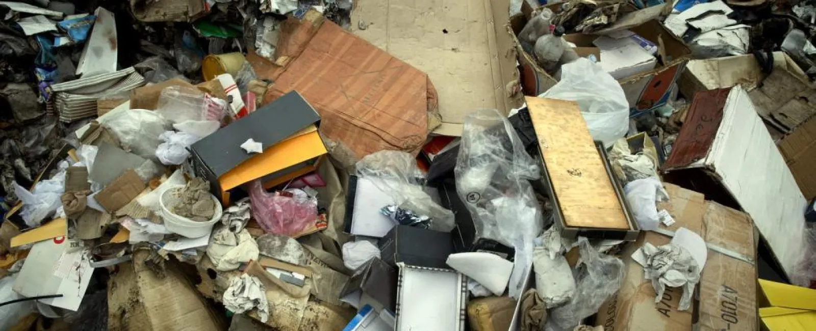 Pile of mixed waste including cardboard, paper, plastic, and other discarded materials in a landfill.