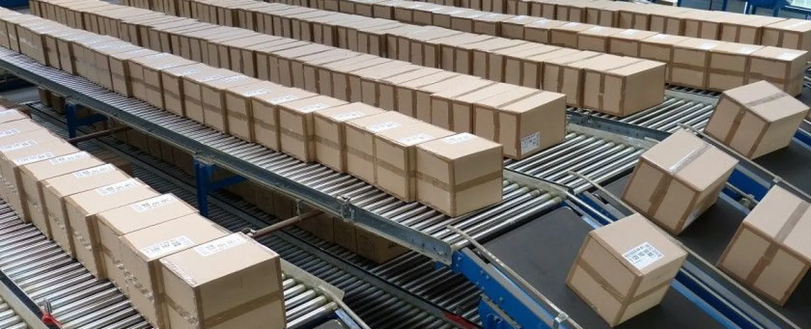 Packaging boxes moving on mechanical conveyor belts inside a large distribution warehouse or fulfillment center.