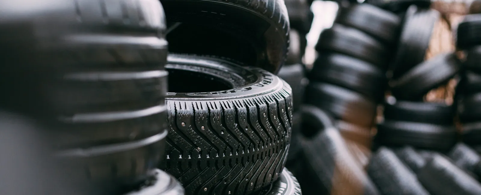 Stacks of various black vehicle tires arranged outdoors in a storage area with blurred background.