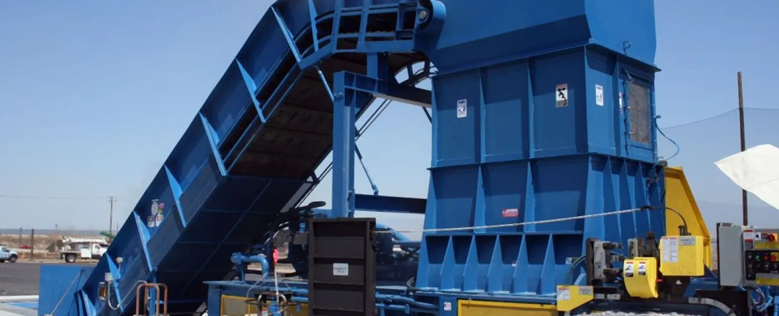 Industrial blue recycling machine compressing and baling aluminum cans outdoors on a clear day