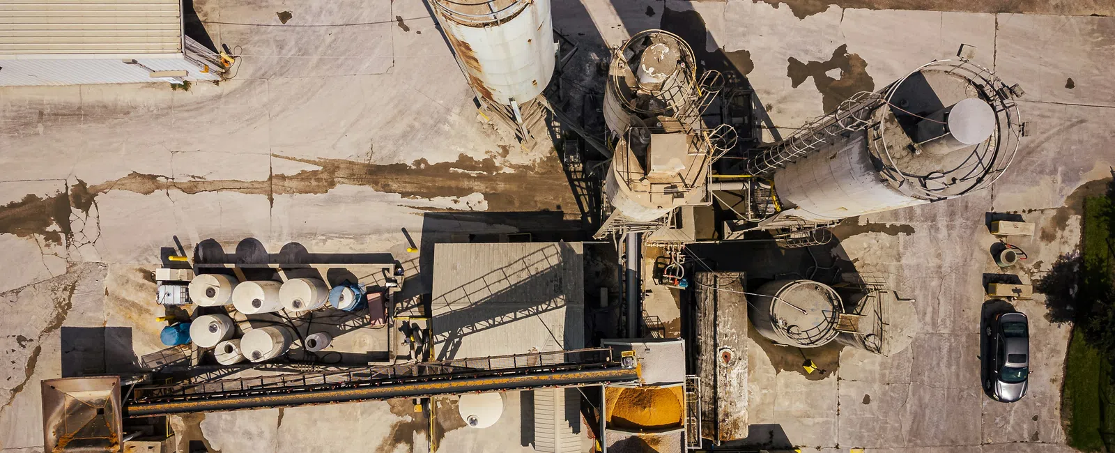 Aerial view of an industrial concrete plant with silos, conveyors, storage tanks, and a parked car.