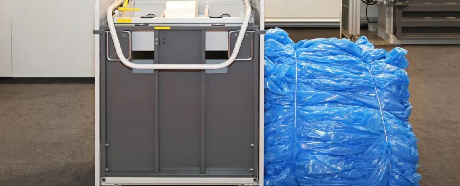 Hospital laundry cart next to a large bundle of blue disposable shoe covers on a gray floor indoors