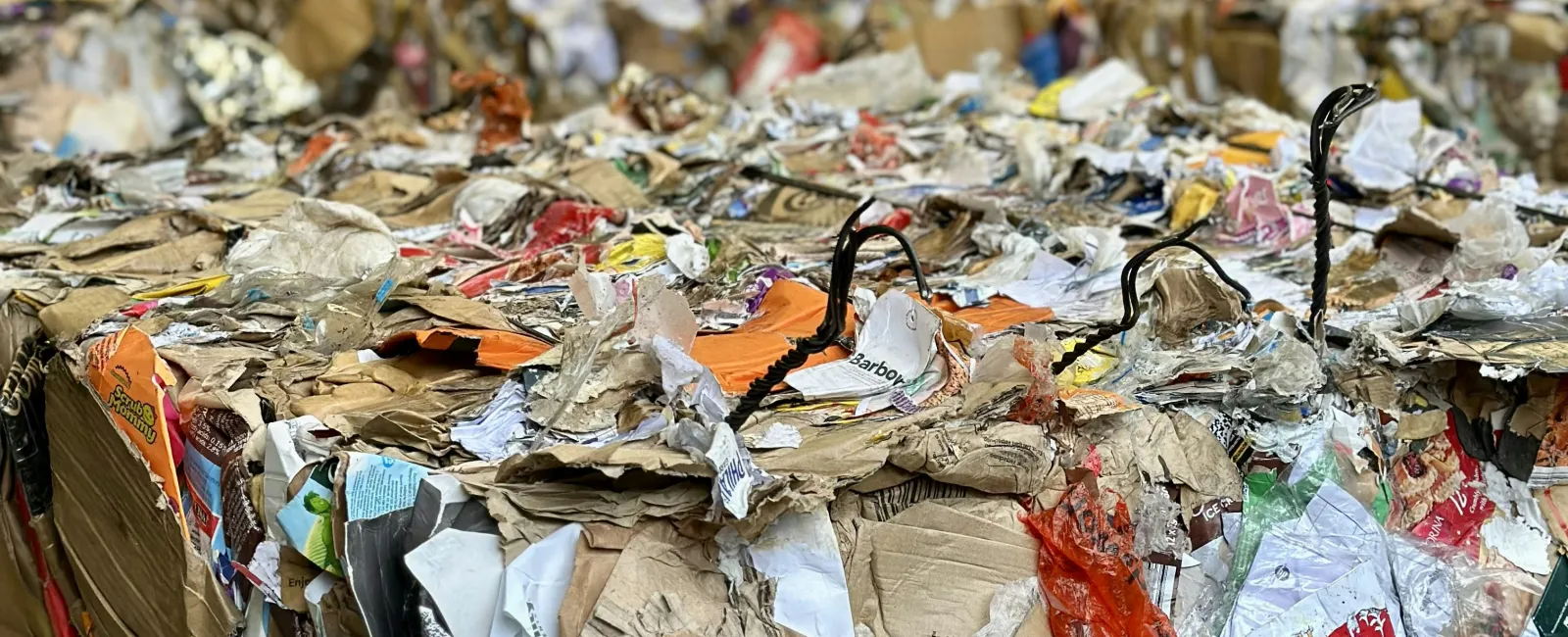 Compressed bales of mixed recyclable paper and cardboard stacked inside a recycling facility warehouse.
