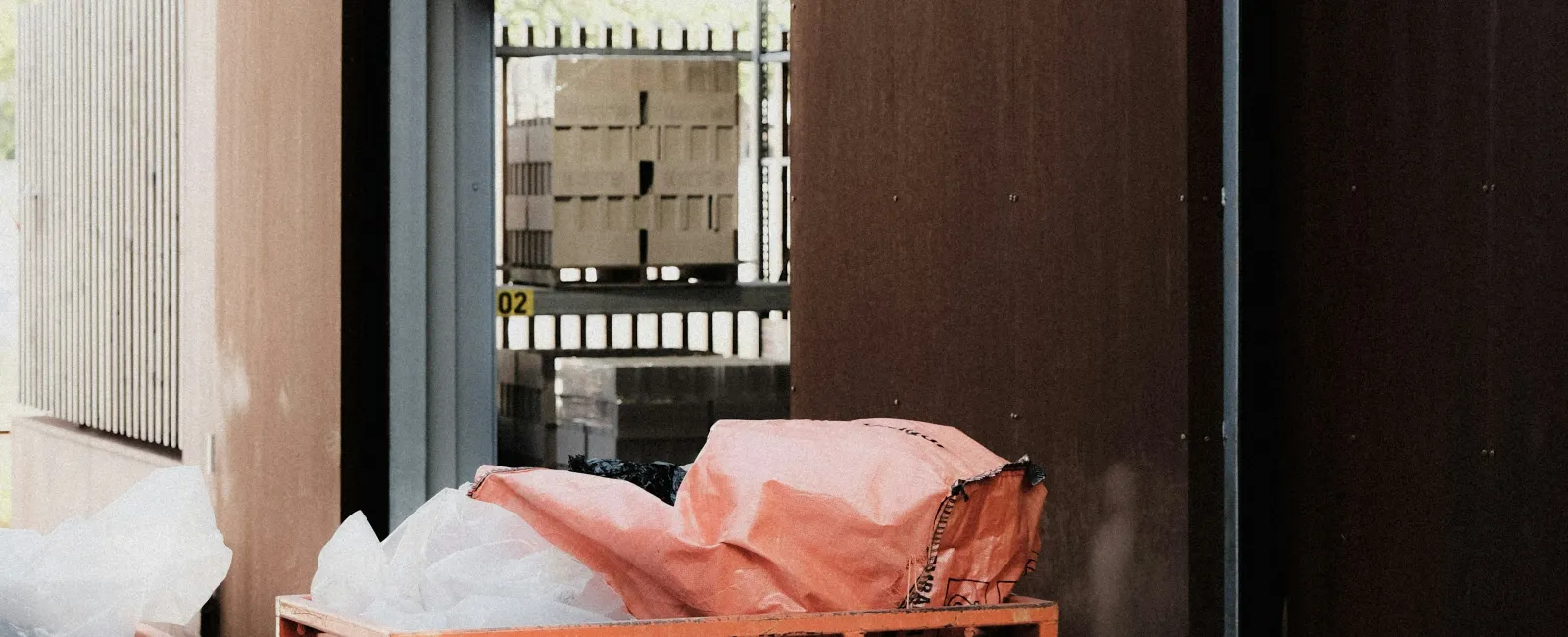 Orange industrial bins filled with plastic bags outside a modern building with wooden and metal paneling.
