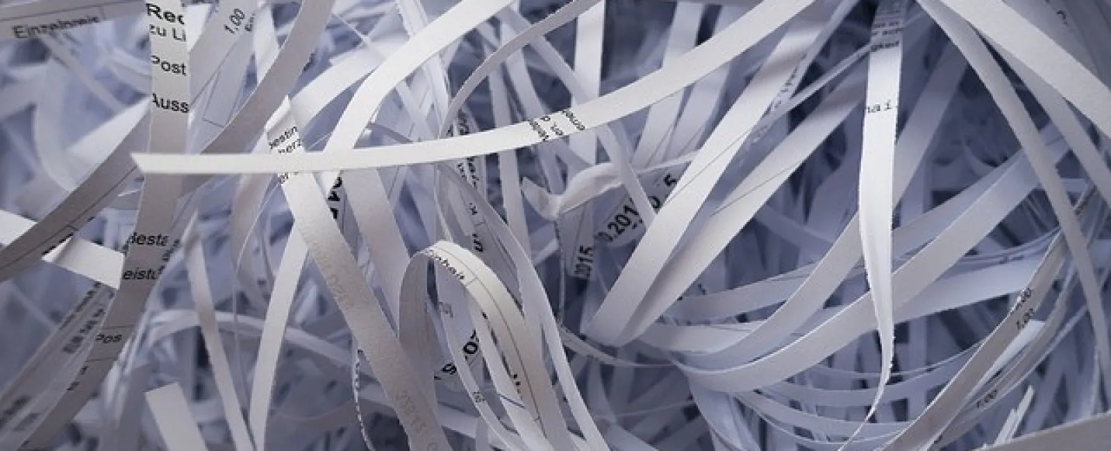 Close-up of tangled shredded white paper strips with printed text, creating a chaotic texture and pattern.