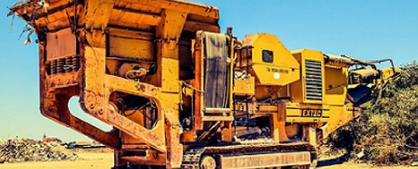 Large yellow industrial wood chipper machine on tracks operating in an outdoor yard with wood debris.
