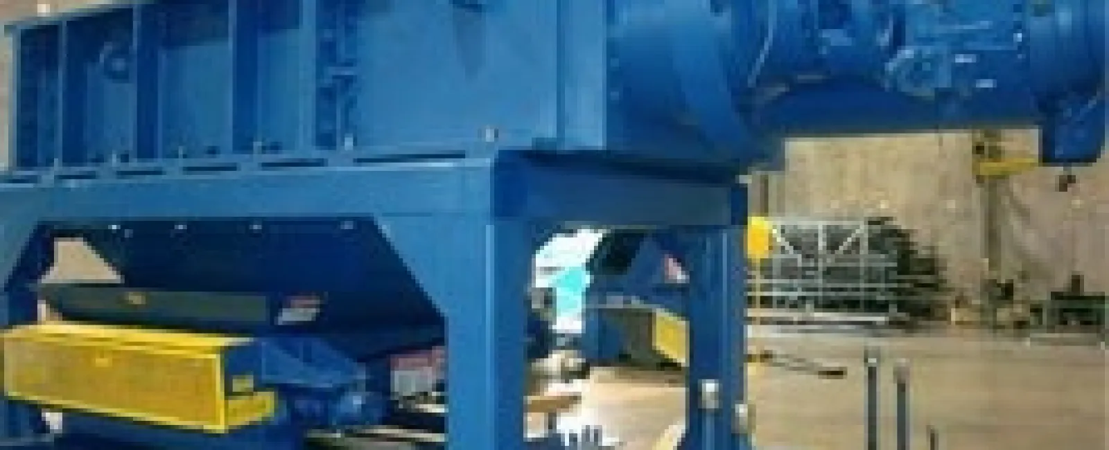 Large blue industrial machine mounted on a platform inside a warehouse or factory setting.