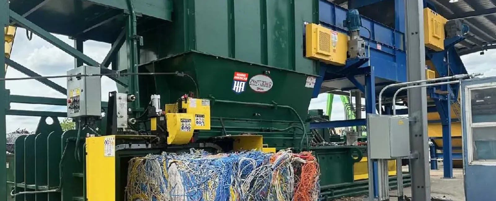 Industrial recycling machine compressing large bale of mixed wires and cables in a factory setting.