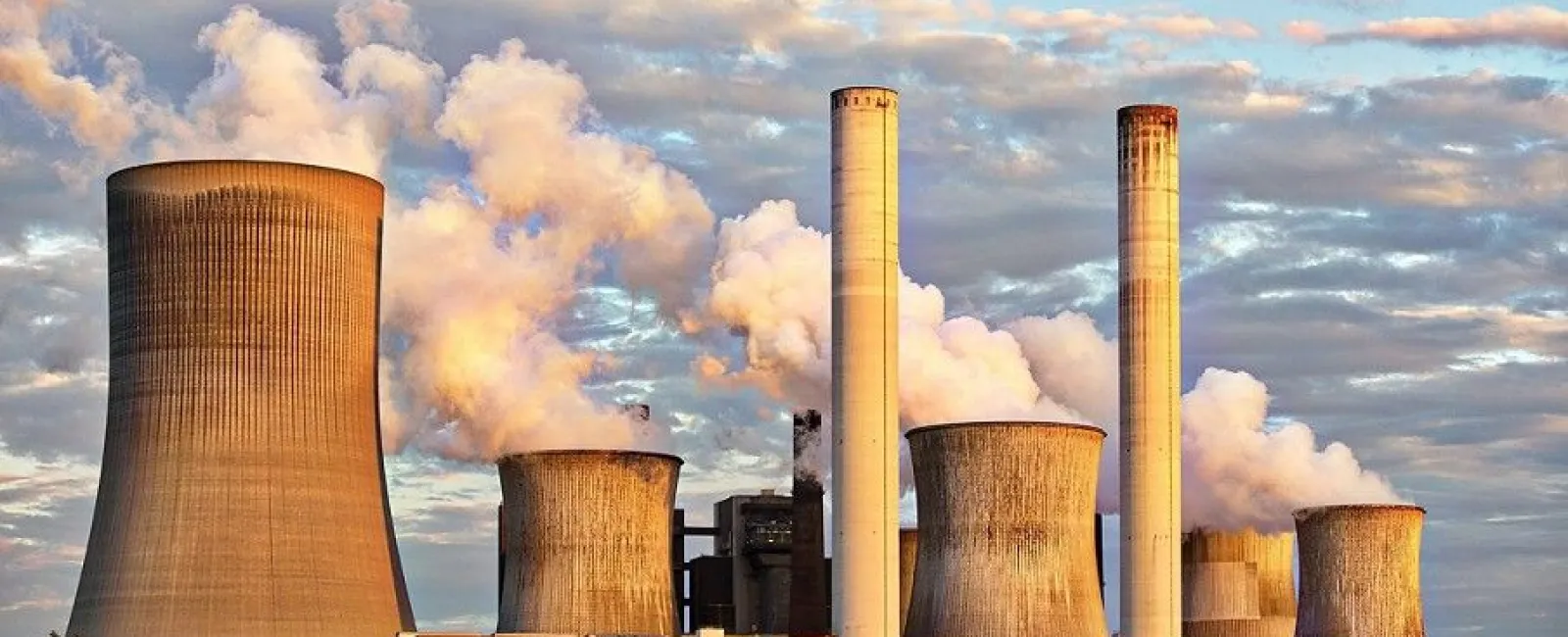 Power plant with large cooling towers emitting steam under a partly cloudy sky at sunset.