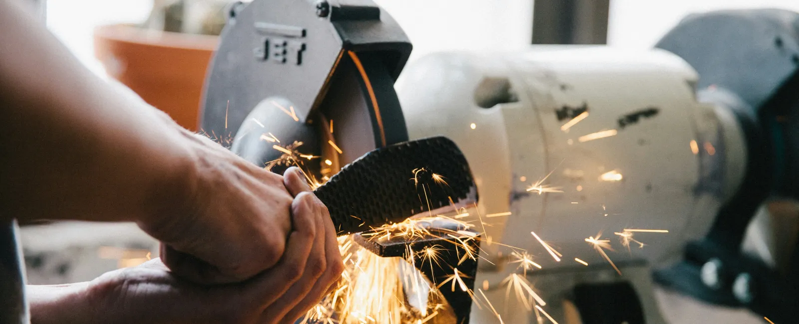 Person sharpening a knife blade with sparks flying from a grinding wheel in a workshop setting