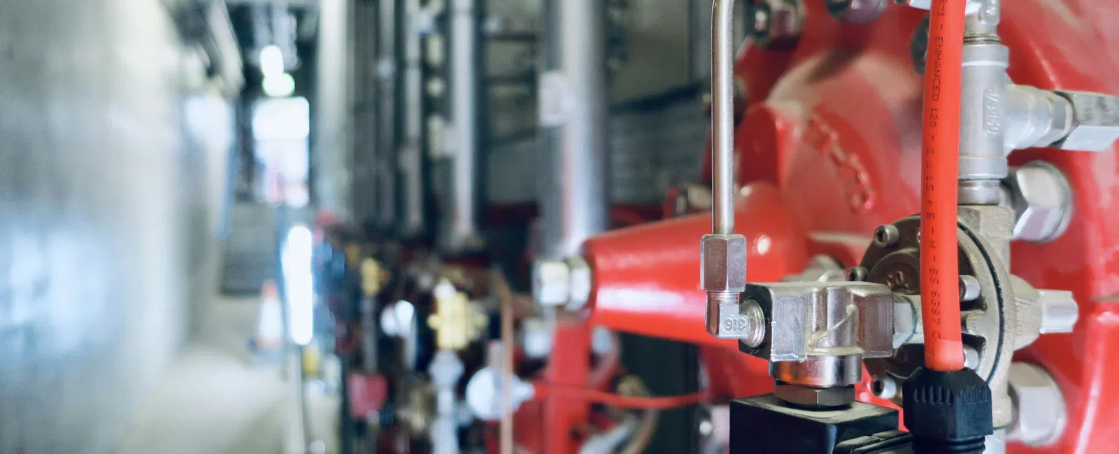 Close-up of industrial red fire safety pipe system with valves and pressure gauges in a mechanical room.