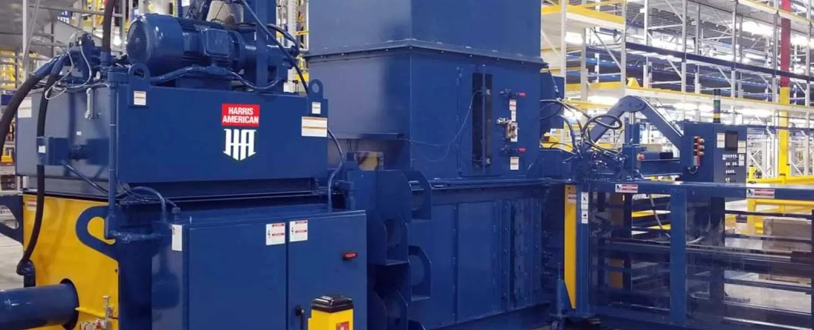 Large blue and yellow industrial machine inside spacious warehouse with metal shelving and concrete floor.