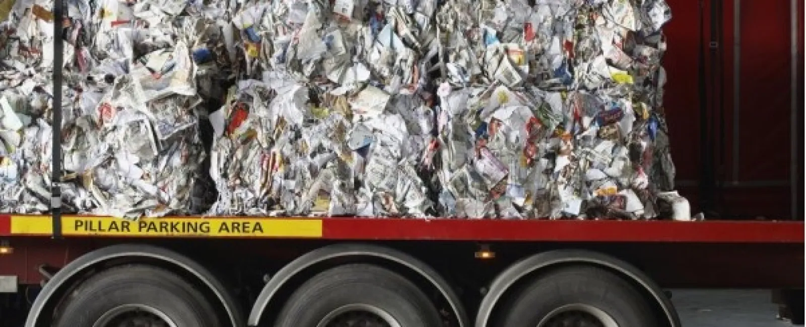 Large bales of compressed recyclable paper stacked on a flatbed trailer inside a warehouse.