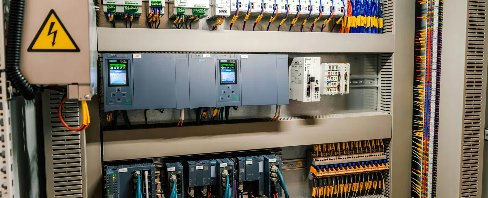 Industrial control panel with wiring, circuit breakers, relays, and programmable logic controllers inside a metal cabinet.
