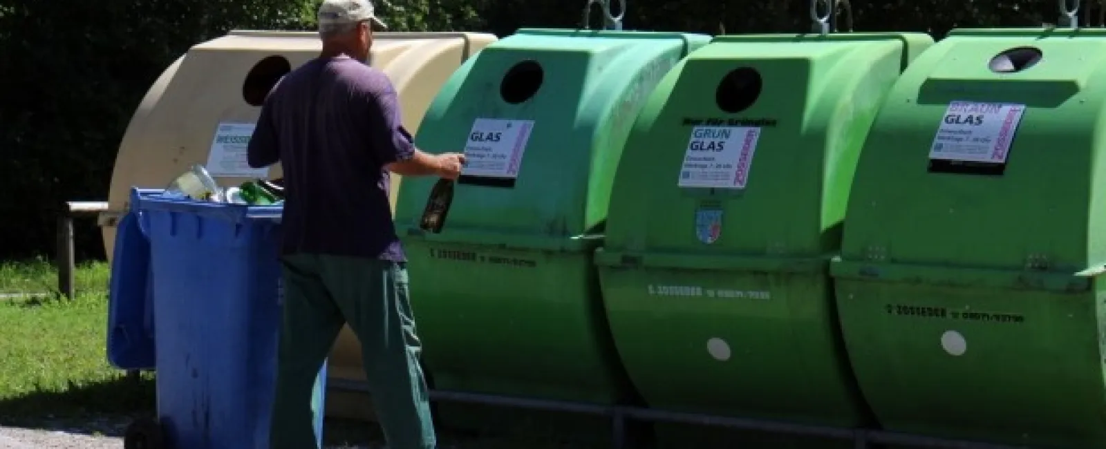 Man recycling glass bottles into green recycling bins outdoors near blue garbage container.