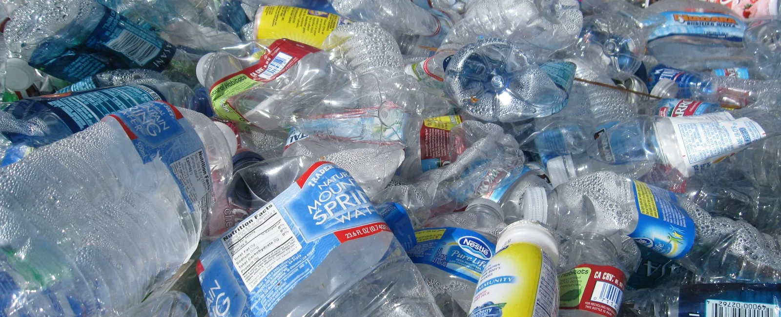 Pile of crushed plastic water bottles and containers with various labels for recycling or waste disposal.