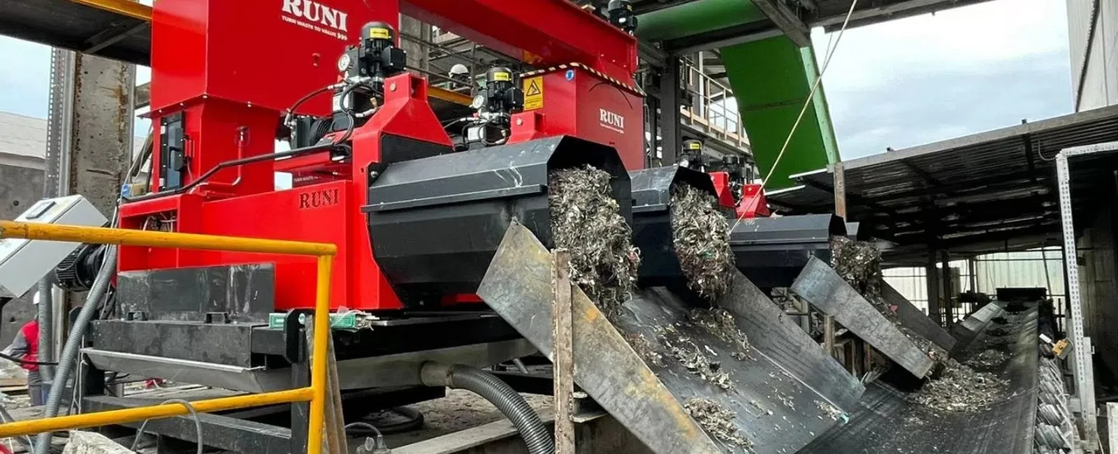 Red RUNI metal shredders processing scrap metal with conveyor belts inside an industrial recycling facility.