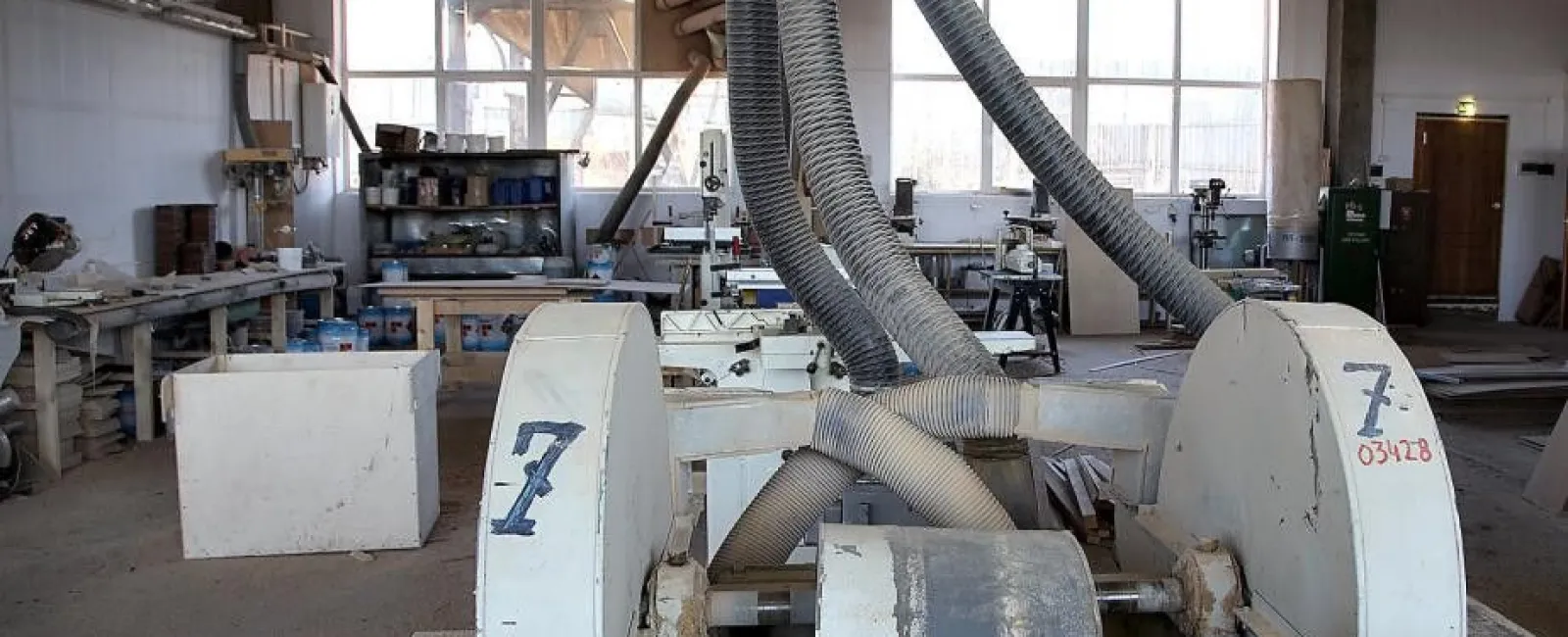 Industrial woodworking machine with dust extraction tubes in a spacious workshop with tools and materials.