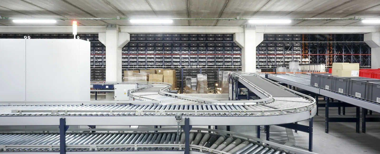 Curved metal roller conveyor system in a spacious warehouse with shelves and boxes in the background.