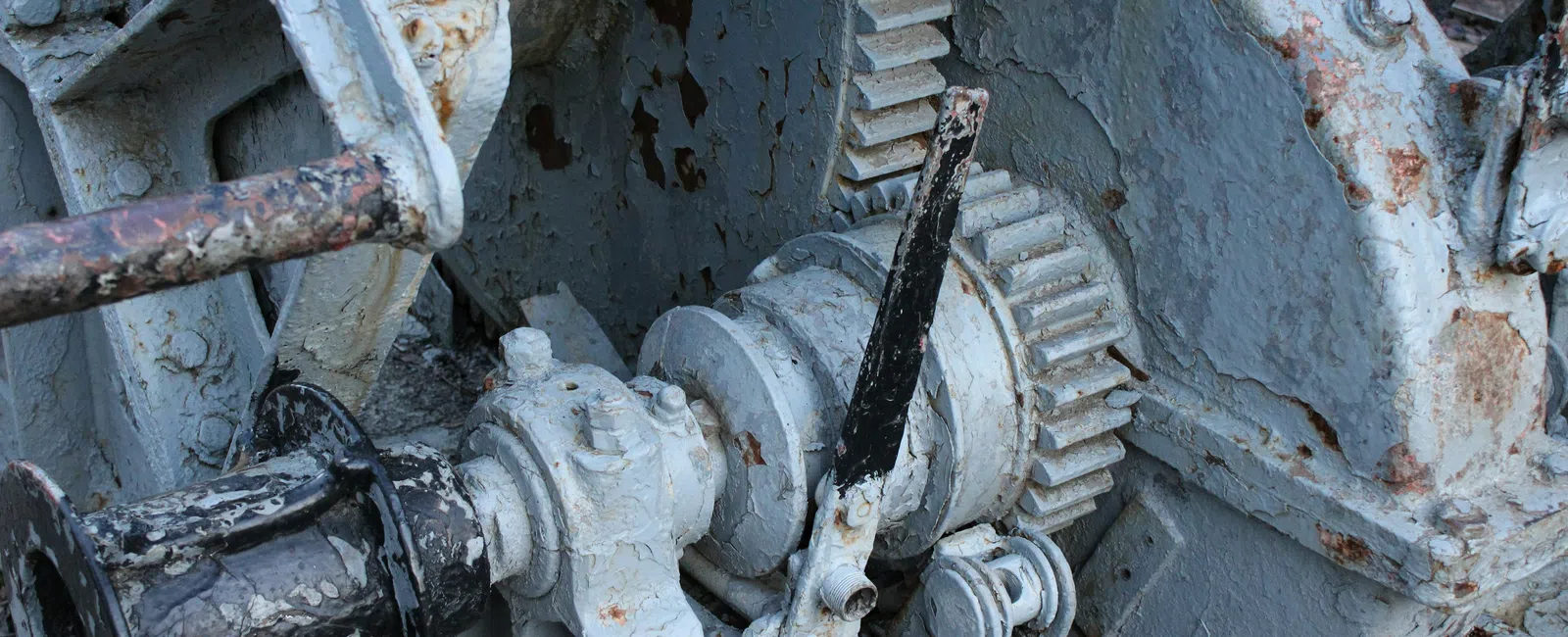 Close-up of rusted metal gears and levers painted gray on old industrial machinery.