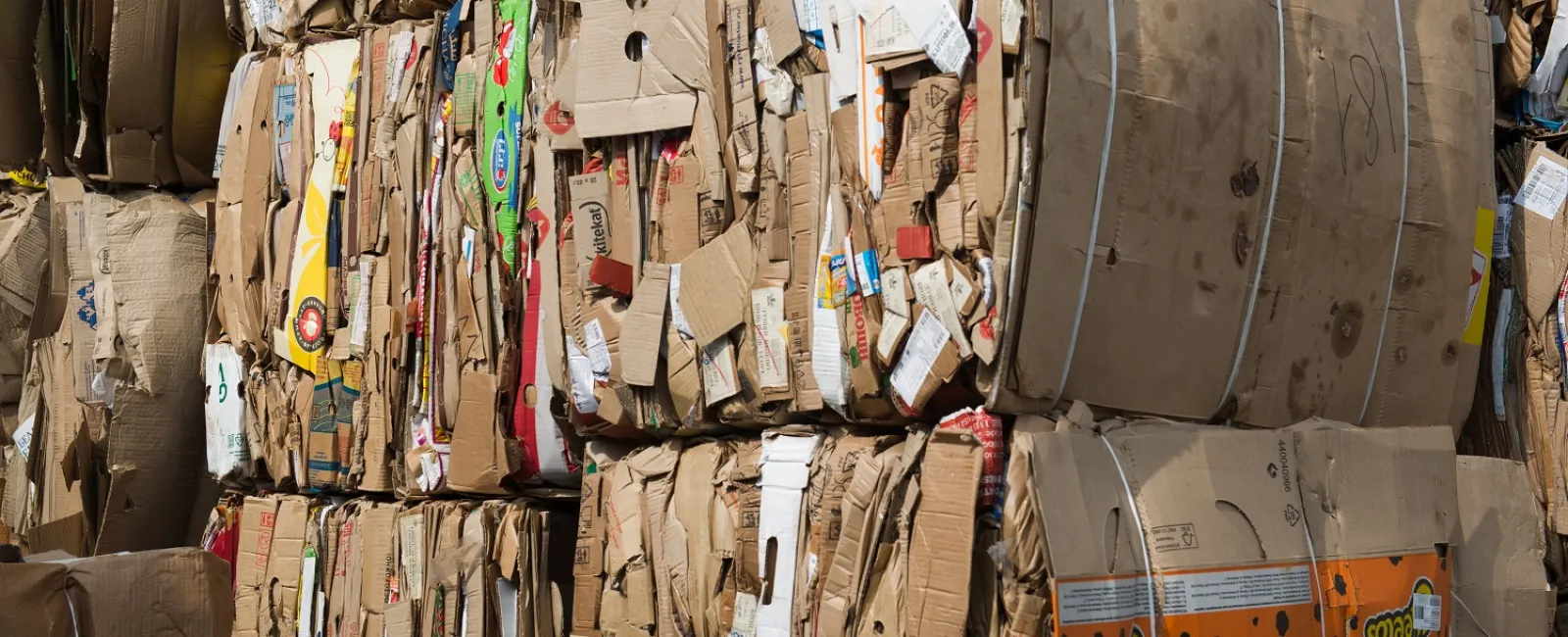 Stacks of compressed cardboard boxes ready for recycling with various printed packaging visible.