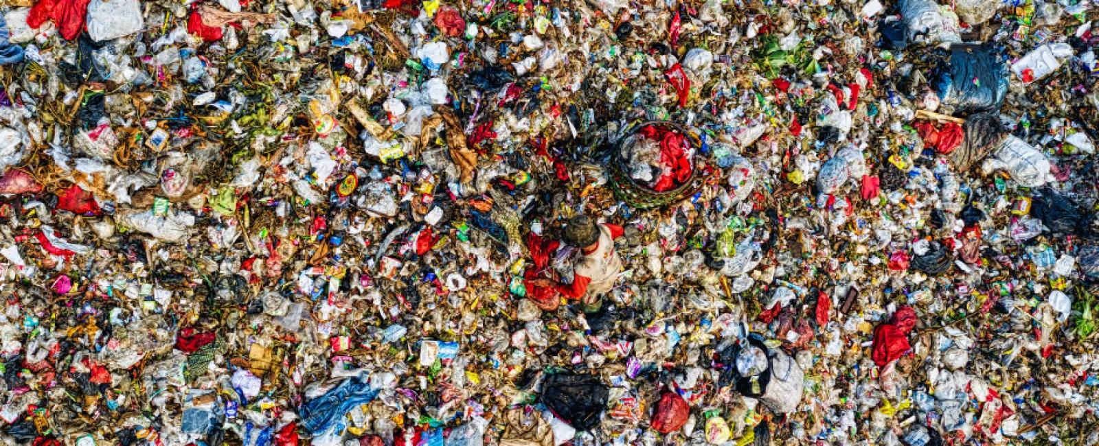 Aerial view of a massive landfill filled with mixed plastic, fabric, and organic waste scattered densely.
