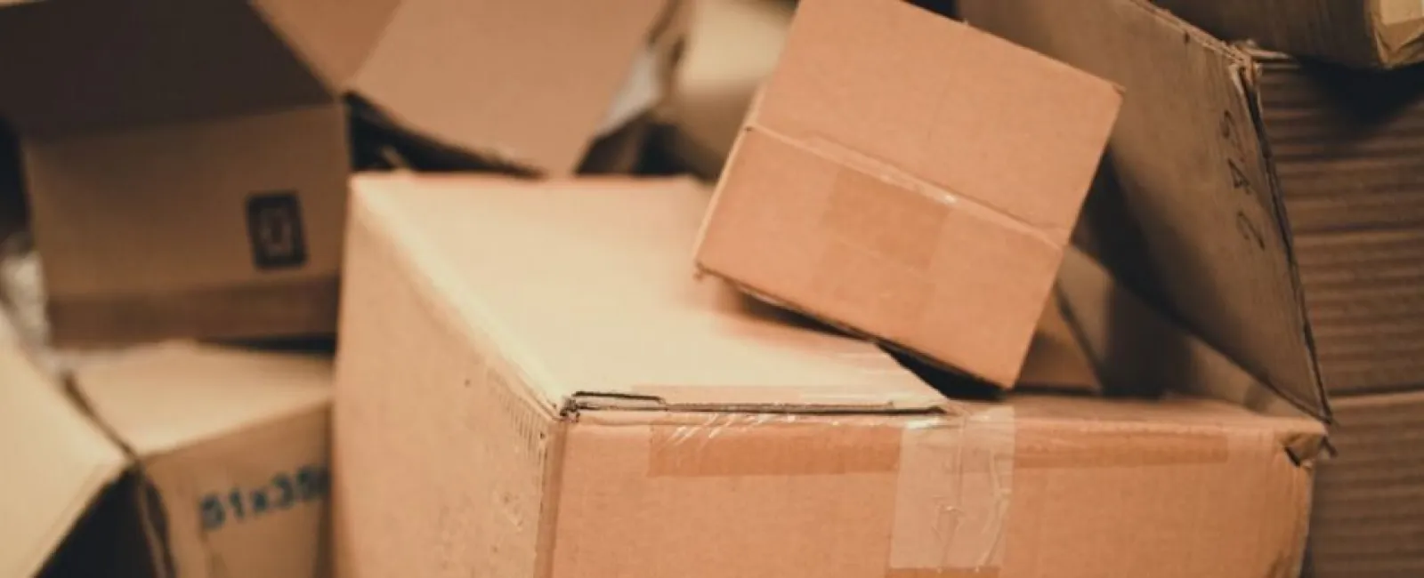 Stack of various cardboard boxes piled together, some open and some closed, in a warm light setting.