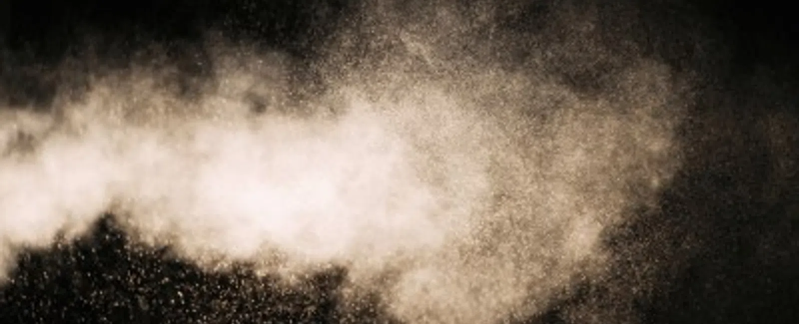Fine powder particles suspended in air forming a cloud against a dark background.