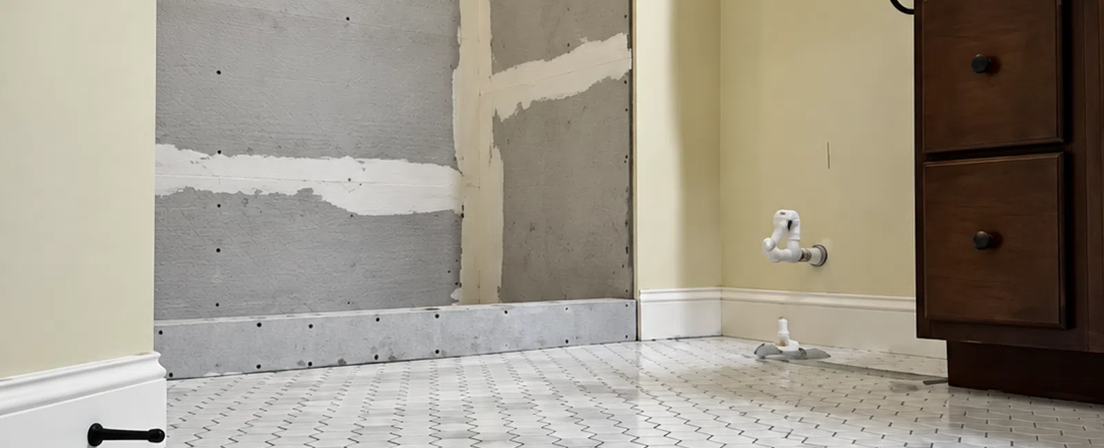 Bathroom under renovation with white hexagonal marble floor tiles, beige walls, and wooden cabinet.