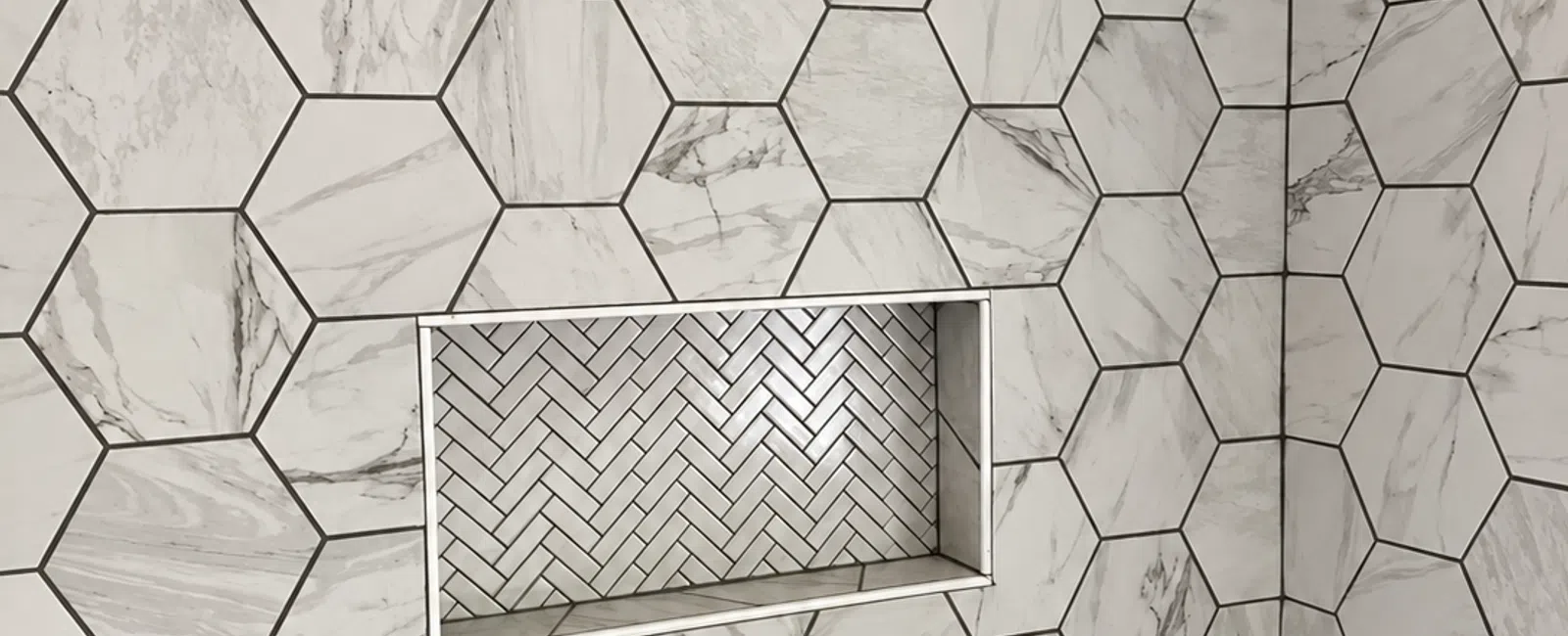 Shower wall with large hexagonal marble tiles and a recessed niche featuring white herringbone tiles.
