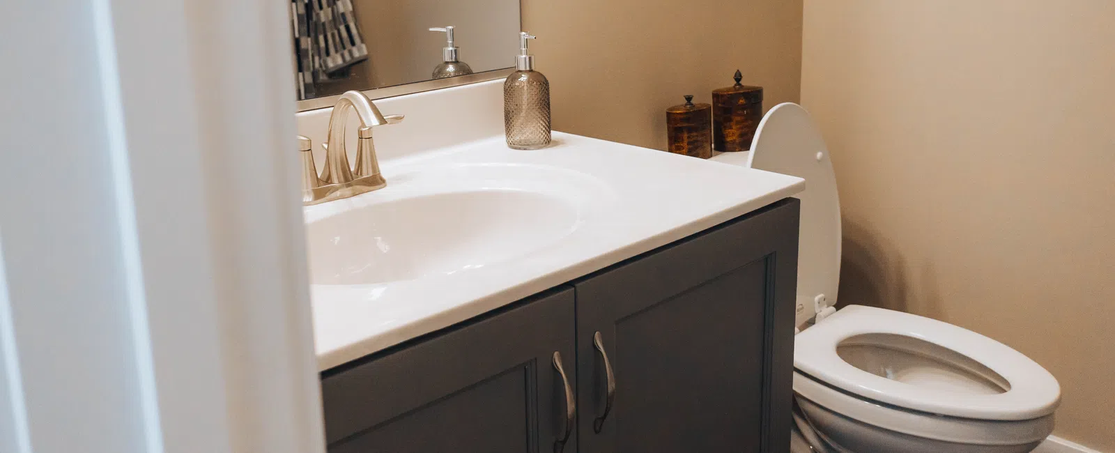 Modern bathroom with white sink and gray vanity next to a white toilet under soft beige walls