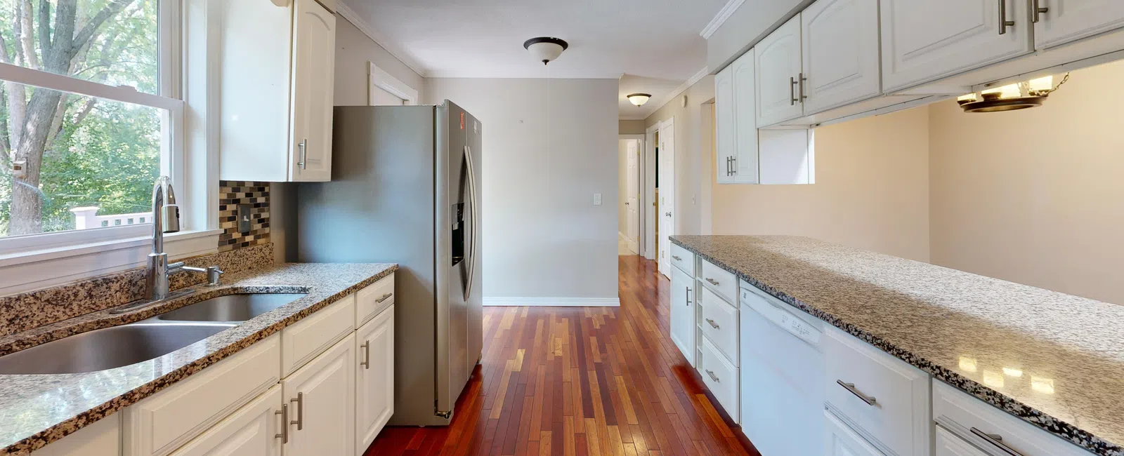 Bright kitchen with white cabinets, granite countertops, stainless steel refrigerator, and hardwood floors.
