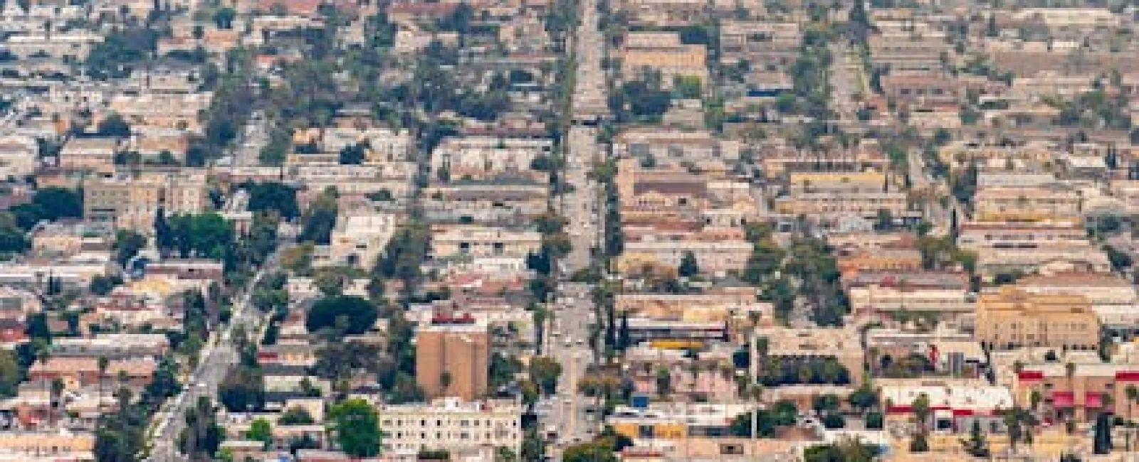 Aerial view of a sprawling urban cityscape with grid-like streets, high-rise buildings, and scattered greenery.