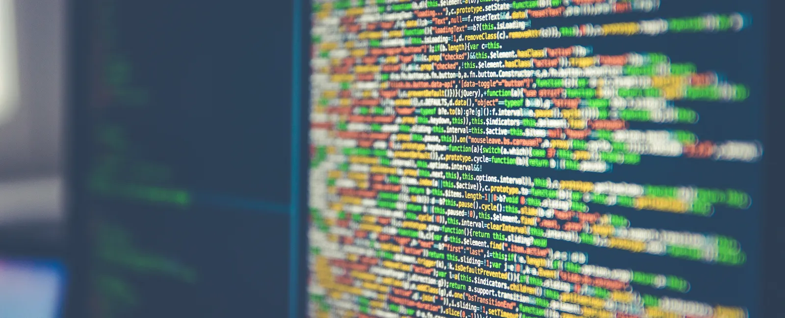 Close-up of colorful computer code lines on a dark screen with blurred background elements in an office.