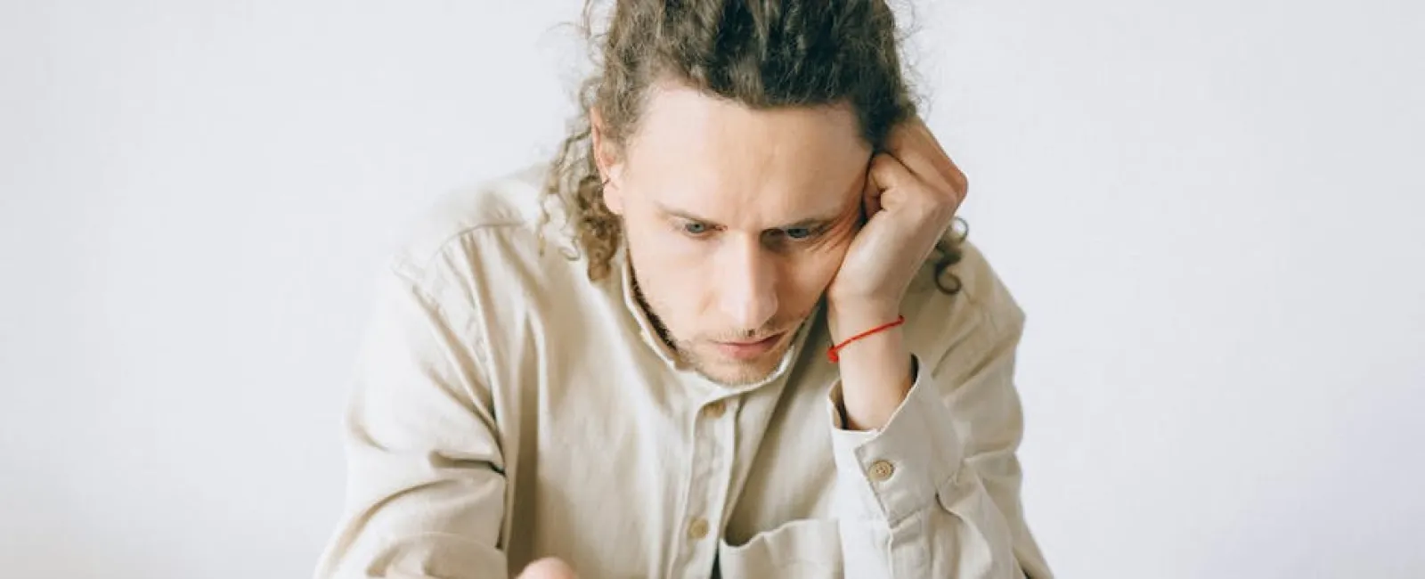 Man with curly hair focused on laptop screen working at a desk with notebooks and papers surrounding him