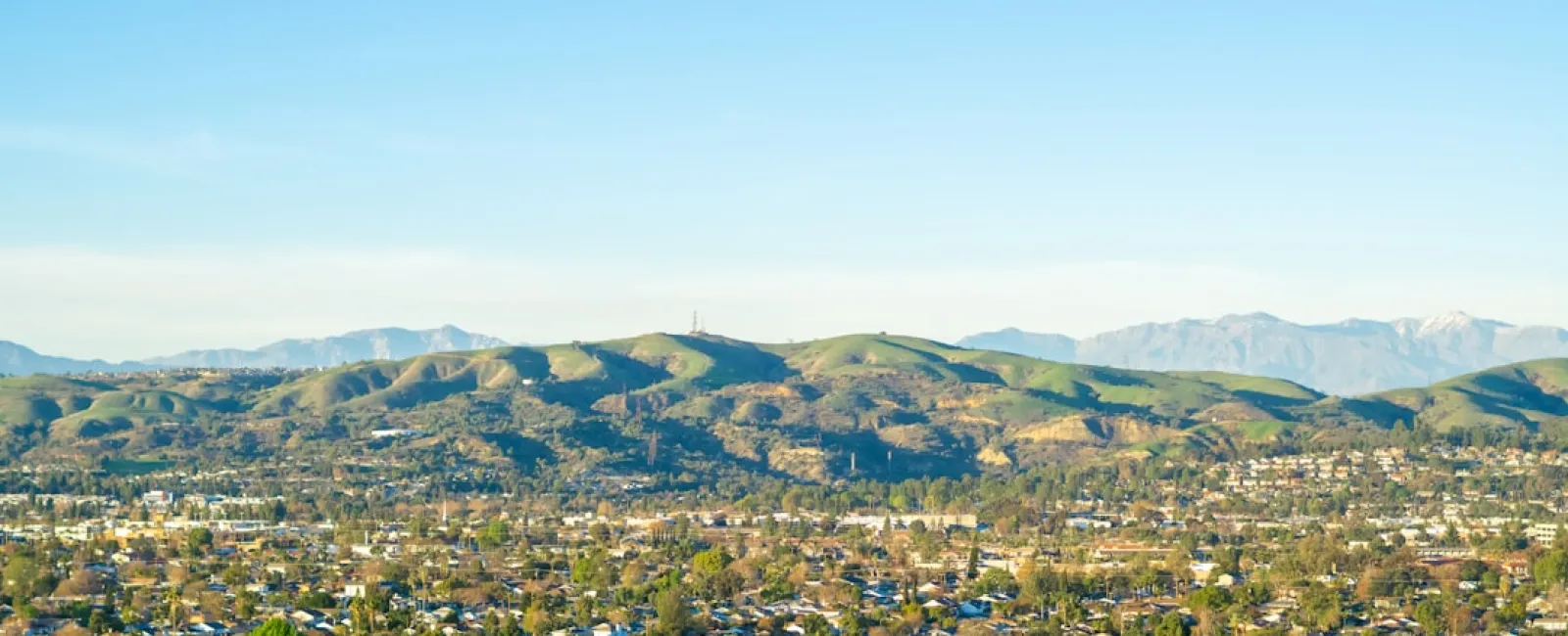 Aerial view of a sprawling suburban area with green hills and mountains under a clear blue sky