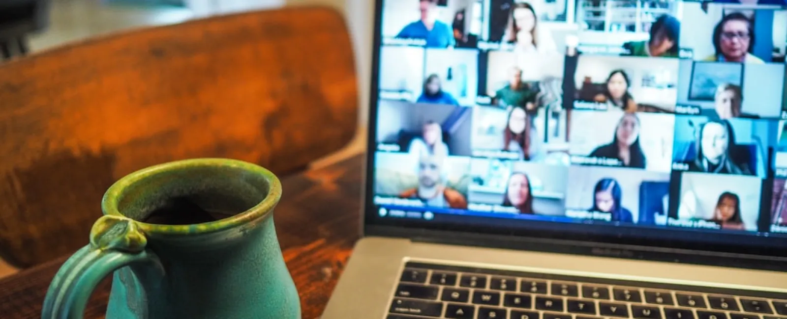 Laptop screen showing a video conference with multiple participants and a green ceramic coffee mug on wooden table