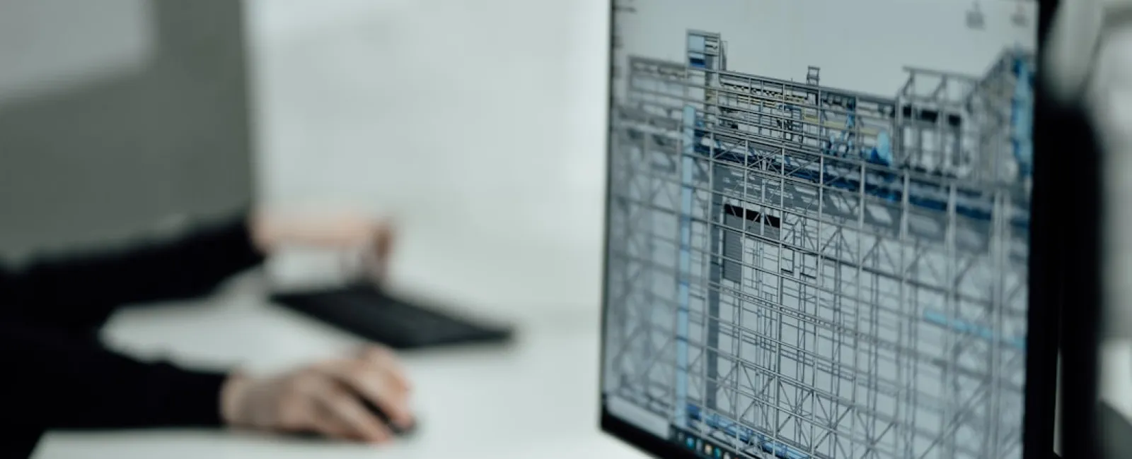 Computer screen displaying detailed 3D architectural scaffolding model with a person working on a keyboard in the background