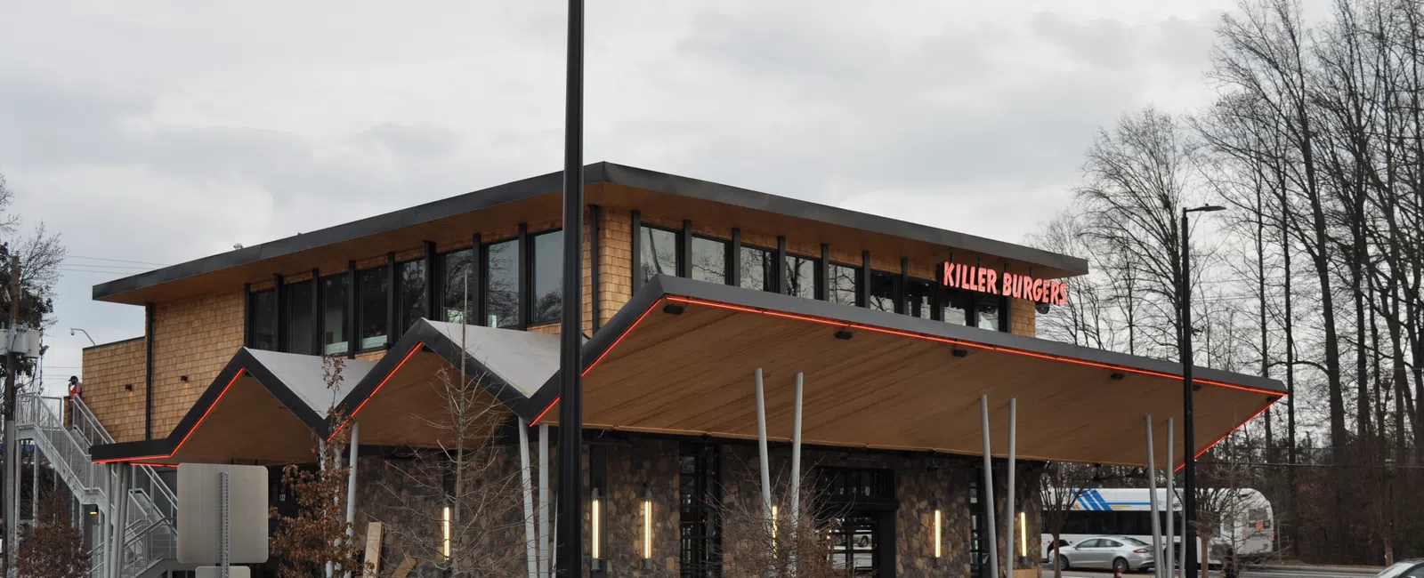 Modern Killer Burger restaurant with sharp angled roof, large windows, and parking lot on a cloudy day
