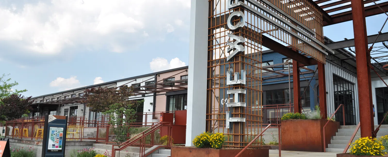 Exterior of a modern building with rust-colored metal structure and stairs under a cloudy sky.