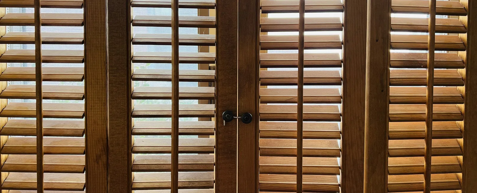 Closed wooden plantation shutters allowing filtered natural light through slats on a window or door.