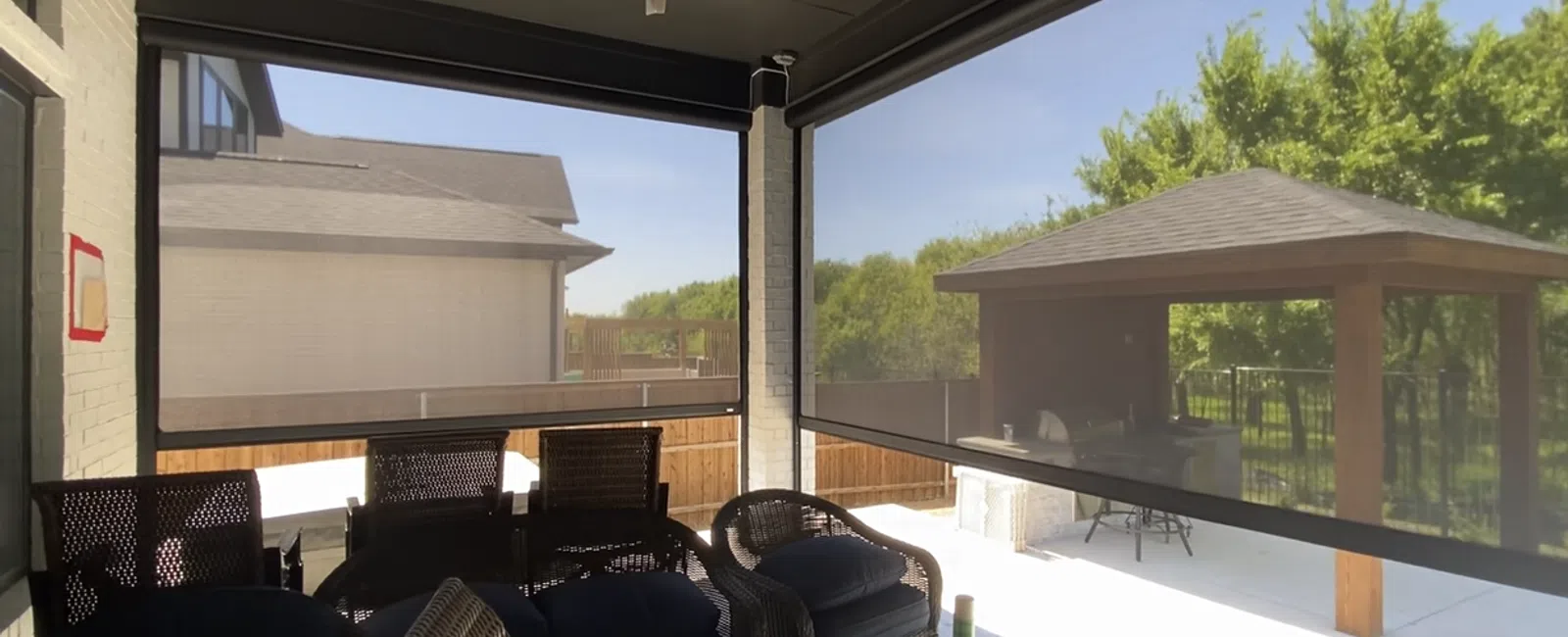Outdoor patio with wicker furniture, ceiling fan, and retractable mesh screens overlooking backyard and gazebo.