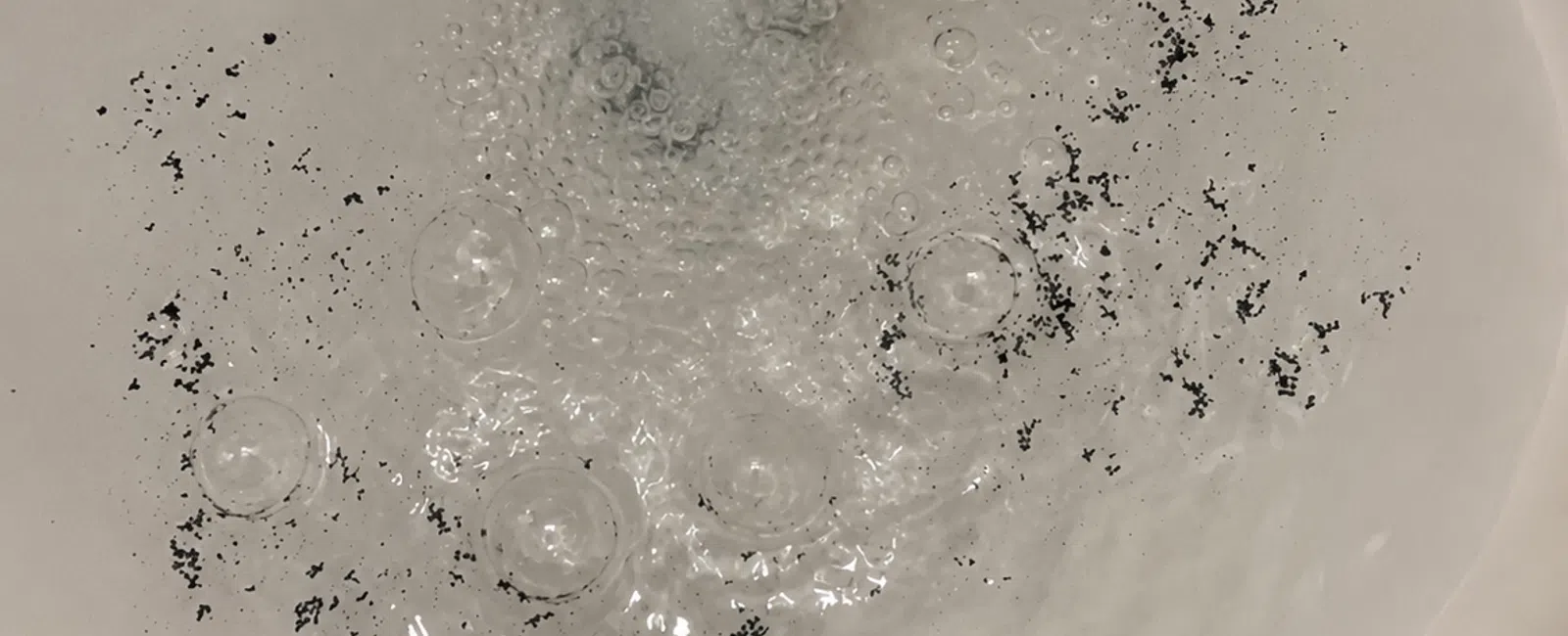 Running water filling a white sink with black debris floating in the water.